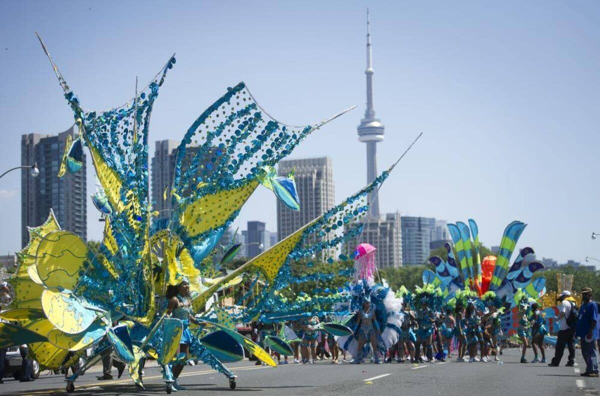 Colour photograph of masqueraders in blue and yellow sequinned costumes on a road with the CN Tower and city towers behind